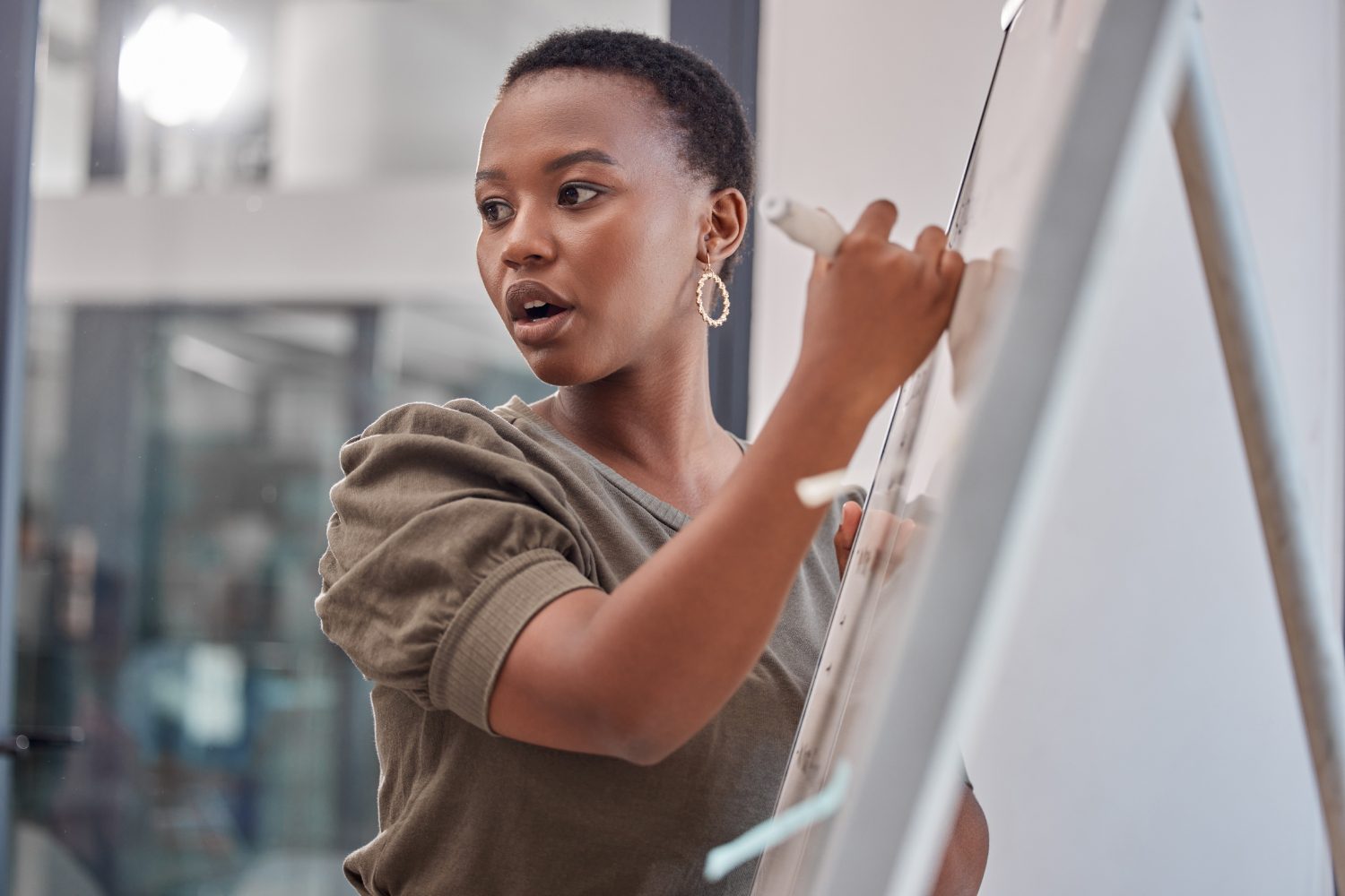 Person writing on a whiteboard while speaking, wearing earrings and a green top.