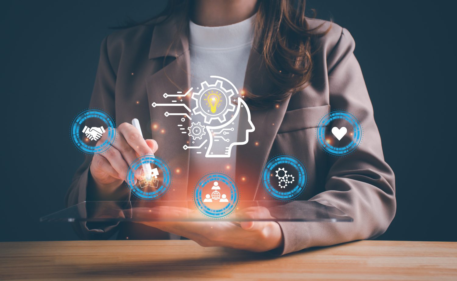 Person touching a tablet displaying futuristic digital icons including a brain with gears, handshake, gear, and lightbulb, suggesting innovation and technology.